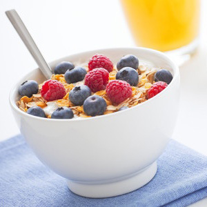 A white bowl full of cereal and milk, topped with raspberries and blueberries, with a glass of orange juice beside the bowl.