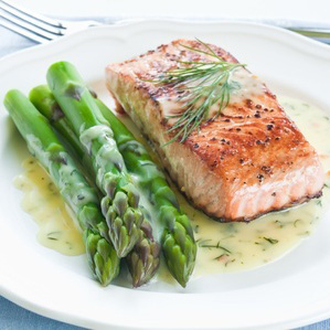 A salmon filet on a white plate at right with asparagus at left.